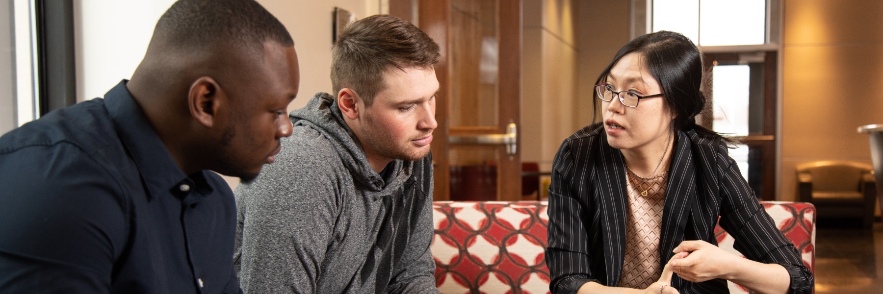 Two students sit at a table with an instructor while looking at laptop computers at IU South Bend.
